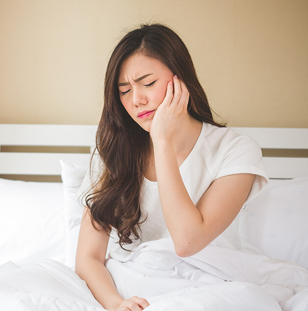 woman sitting up in bed and holding her jaw in pain